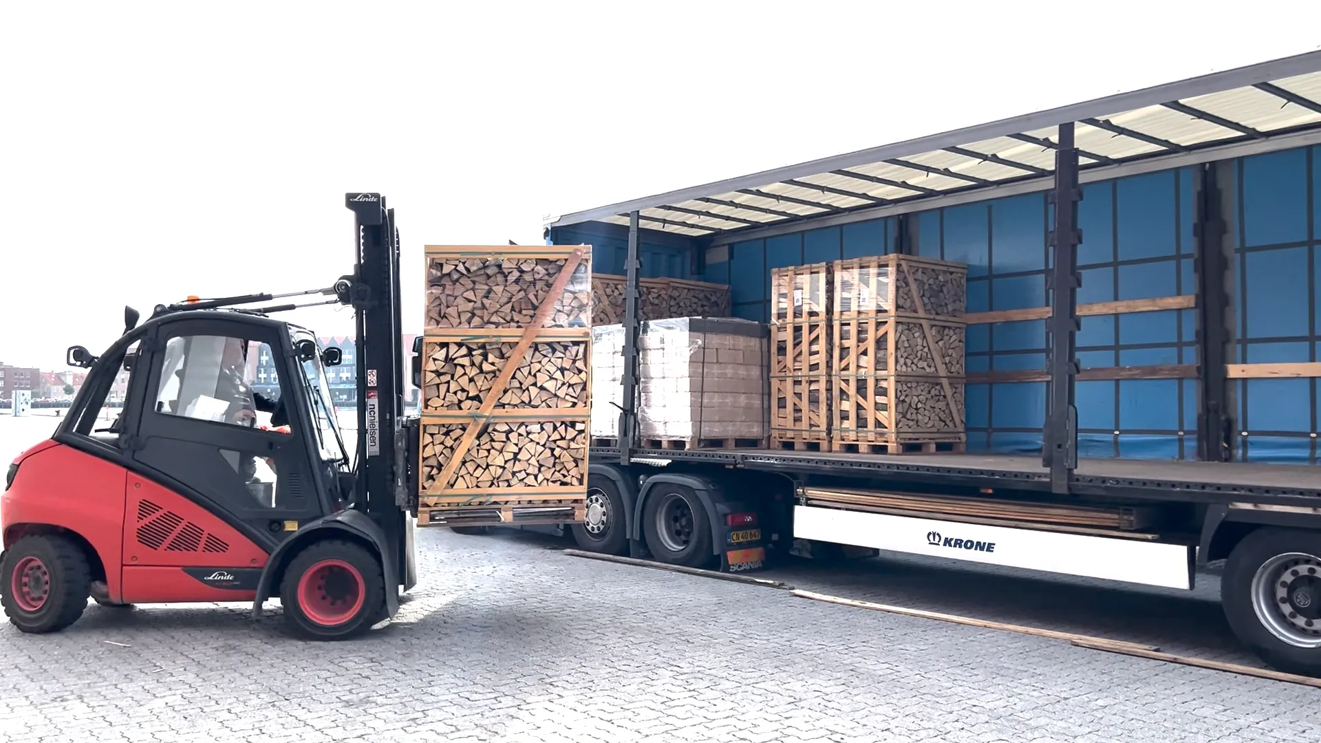 Forklift loading crates of firewood onto a curtain-side trailer